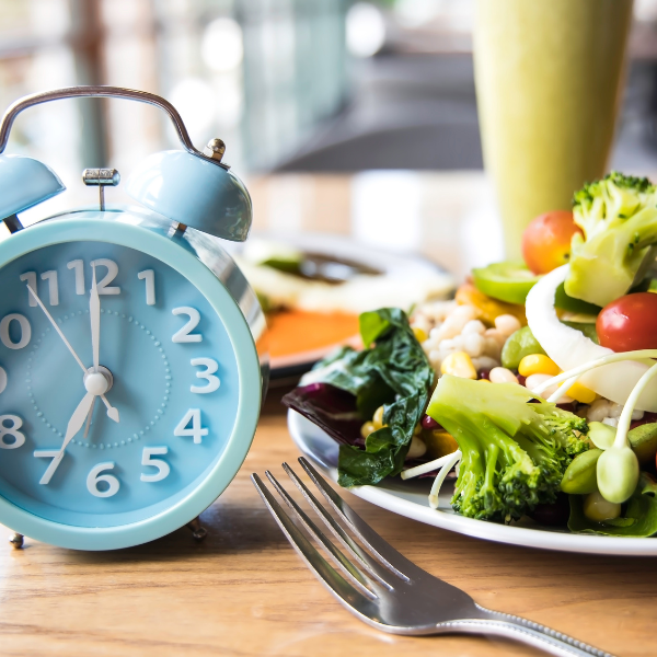 Réveil bleu vintage à côté d'une assiette de salade fraîche et colorée, symbolisant le jeûne intermittent